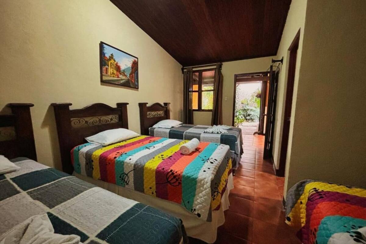 Ein Zimmer mit drei Betten, einer Holzbalkendecke, einem Bild an der Wand und Blick ins Freie.