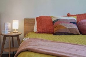 A bed with a quilted headboard, a bedside table with a lamp, and a sign on the wall.