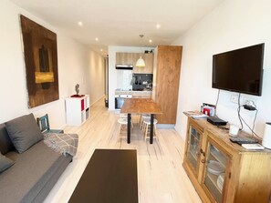 Ein kompakter Wohnbereich mit Sofa, Esstisch, Küchenzeile und an der Wand montiertem Fernseher.