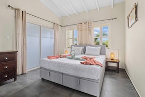 A bedroom with a bed, a dresser, a window with curtains, and a view of greenery outside. - Caribbean Club 111 Parrots Perch on a small-scale resort with beautiful views (Kralendijk)