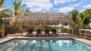 Une piscine dotée de chaises longues et d’une structure recouverte d’un toit de chaume.
