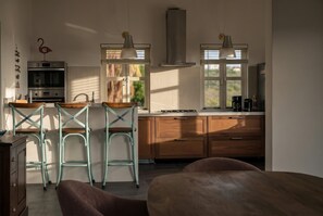 A modern kitchen with a central island, bar stools, a built-in oven, and a coffee maker. - Caribbean Club 111 Parrots Perch on a small-scale resort with beautiful views (Kralendijk)