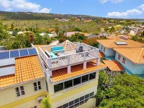 A residential building with a balcony, solar panels, and a view of a green landscape. - Caribbean Club 111 Parrots Perch on a small-scale resort with beautiful views (Kralendijk)