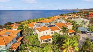 Un quartier résidentiel situé sur la côte, où les maisons se distinguent par leurs toits recouverts de tuiles rouges, leurs panneaux solaires et leur végétation luxuriante.