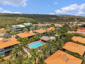 A residential area with houses, a swimming pool, and a hilly landscape in the background. - Caribbean Club 111 Parrots Perch on a small-scale resort with beautiful views (Kralendijk)