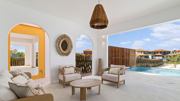 Ampla sala de estar com piscina, apresentando uma mesa de madeira redonda, dois sofás e um lustre.