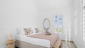 Quarto com cama, mesa de cabeceira, espelho e janela com persianas.