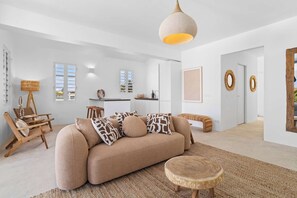 A spacious living room with a beige sofa, a round wooden coffee table, and a woven rug. There is a dining area with a white table and chairs, and a kitchen in the background. - Laguna Serena Villa stylishly furnished villa with a large outdoor space and a private pool (Kralendijk)