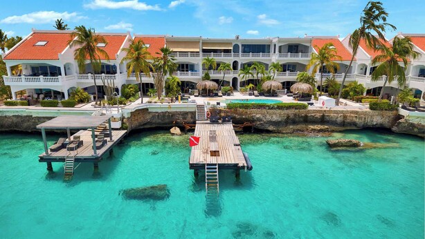 A resort with a pool, multiple balconies, and a dock extending into clear turquoise water. - Apartment Belmar 6 with a beautiful view and refreshing shared pool (Kralendijk)