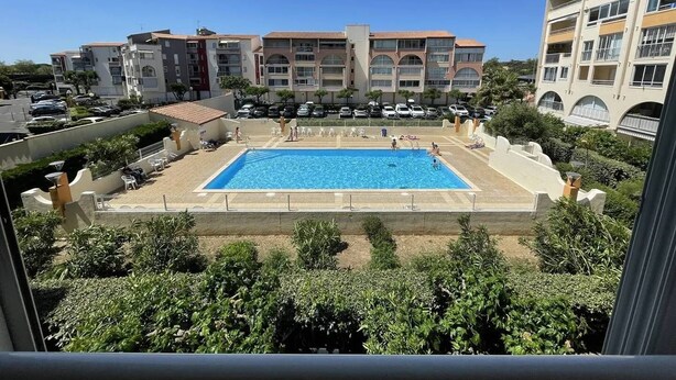 Ein Pool, umgeben von viel Grün, mit mehrstöckigen Gebäuden im Hintergrund.