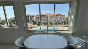 Ein Zimmer mit einem großen Fenster, einem runden Tisch und weißen Plastikstühlen.