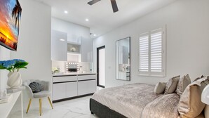 Une chambre à coucher moderne avec un grand lit, une coiffeuse avec éclairage, un miroir et une vue sur la cuisine.