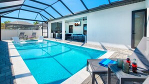 Une piscine avec des chaises longues, une table avec des bouteilles et un patio couvert.