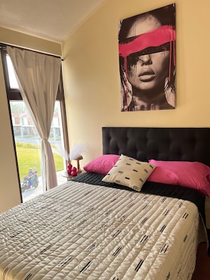 Une chambre à coucher avec un grand lit, une tête de lit, une fenêtre avec des rideaux et une œuvre d’art accrochée au mur.