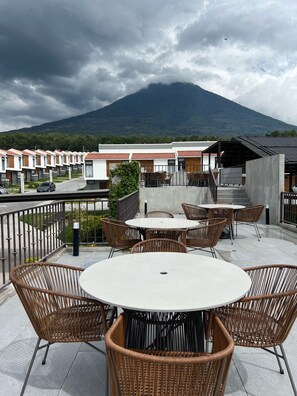 A terrace with wicker chairs and tables, overlooking a mountain and a row of buildings. - Quite 3-bedroom condo in a Secure Gated Community,Perfect view of all 3 Volcanos (Guatemala. Sobre la)