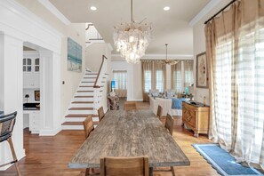 A spacious dining area with a wooden table and chairs, a chandelier, and a staircase leading to another level. - Casa Del Mare Caribe (Miramar Beach)