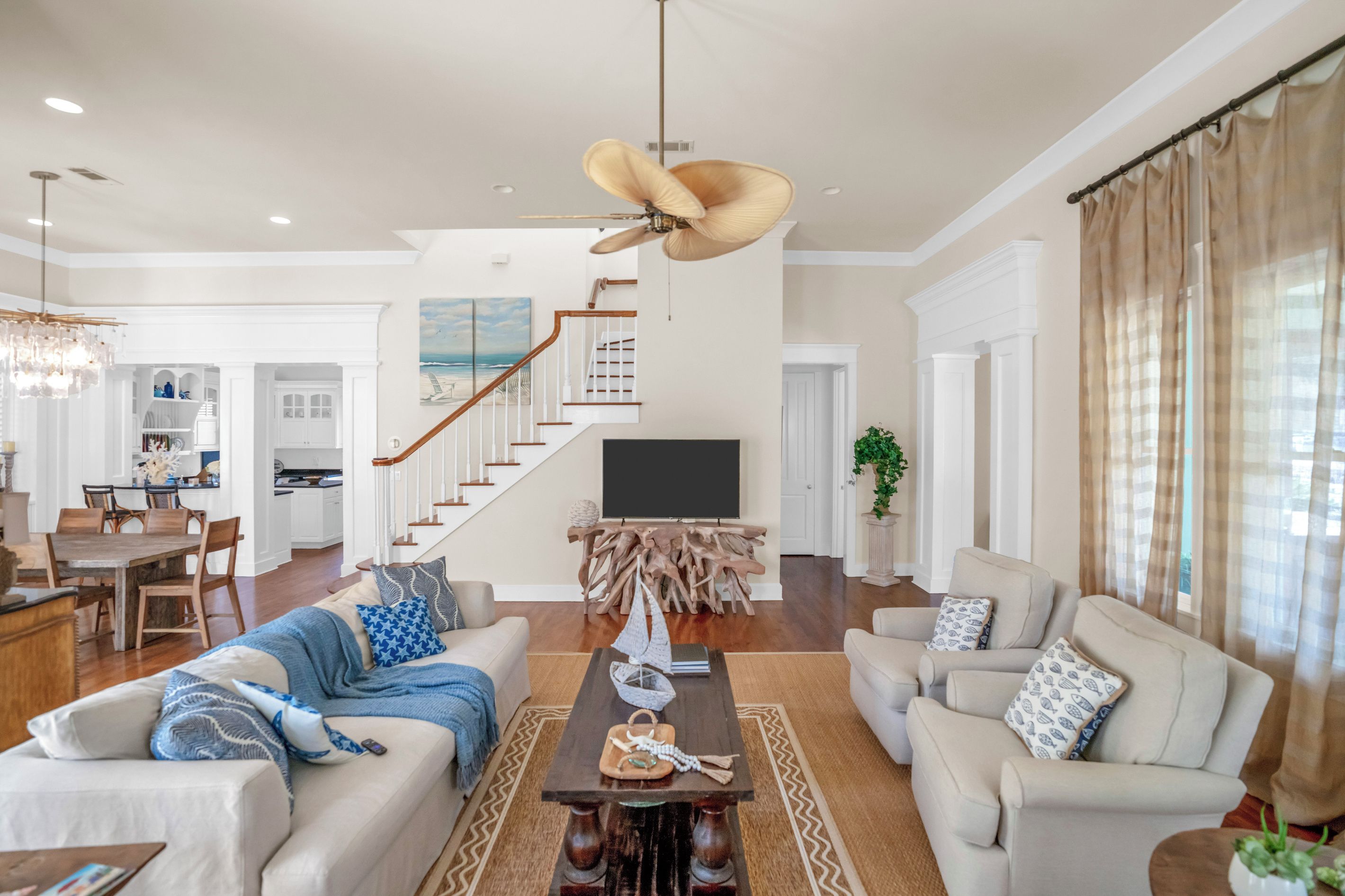 A spacious living room with a high ceiling fan, a dining area with a wooden table and chairs, and a kitchen in the background.