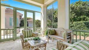 Estar coberto com móveis de vime, uma mesa de vidro e vista para casas vizinhas.