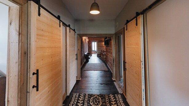 A wooden hallway with a patterned rug, a hanging light fixture, and a view into another room. - Historic Loft Stay Near Mammoth Cave National Park (Cave City)