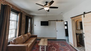 A room with a ceiling fan, a sofa, a small table, a patterned rug, and a door leading to another room. - Historic Loft Stay Near Mammoth Cave National Park (Cave City)