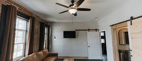 A room with a ceiling fan, a sofa, a small table, a patterned rug, and a door leading to another room.