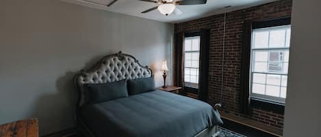Ein Schlafzimmer mit einer karabinierten Kopfteil, einem Bett, einem Nachttisch mit Lampe, einem Fenster mit Aussicht und einem Deckenventilator.