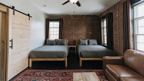 A room with two beds, a ceiling fan, a brick wall, and a large window. - Historic Loft Stay Near Mammoth Cave National Park (Cave City)