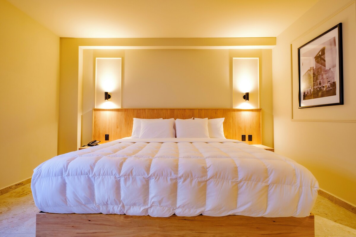 A hotel room with a large bed, wooden headboard, two bedside lamps, and a framed picture on the wall.