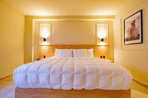 A hotel room with a large bed, wooden headboard, two bedside lamps, and a framed picture on the wall.