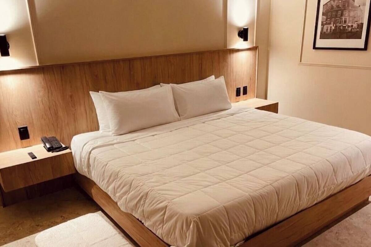 Habitación de hotel con una cama grande, cabecera de madera, mesitas de noche con lámparas, un cuadro en la pared y un teléfono en la mesita de noche.