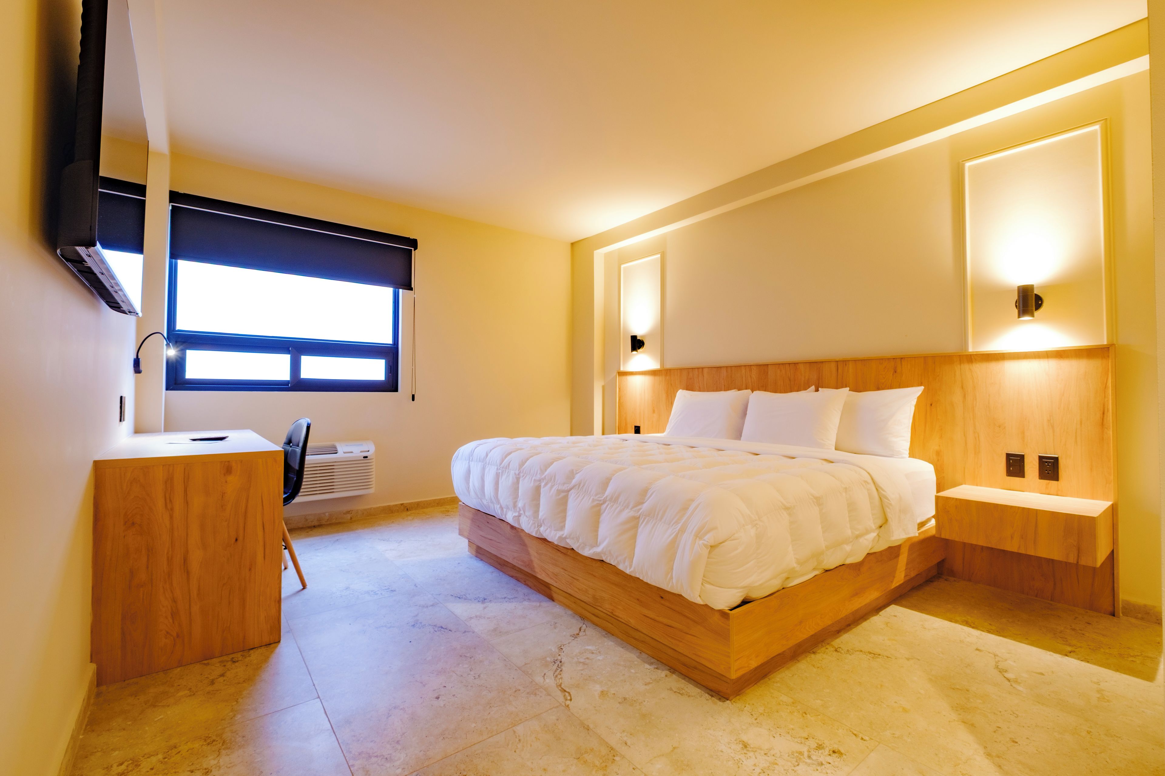 A modern bedroom with a large bed, bedside tables, a desk, and a chair.