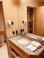 Un baño con encimera de granito, un lavamanos, un espejo y dos secadores de pelo fijos en la pared.