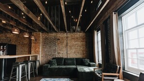A room with exposed brick walls, a wooden ceiling, a sofa, a coffee table, and a bar area with stools.