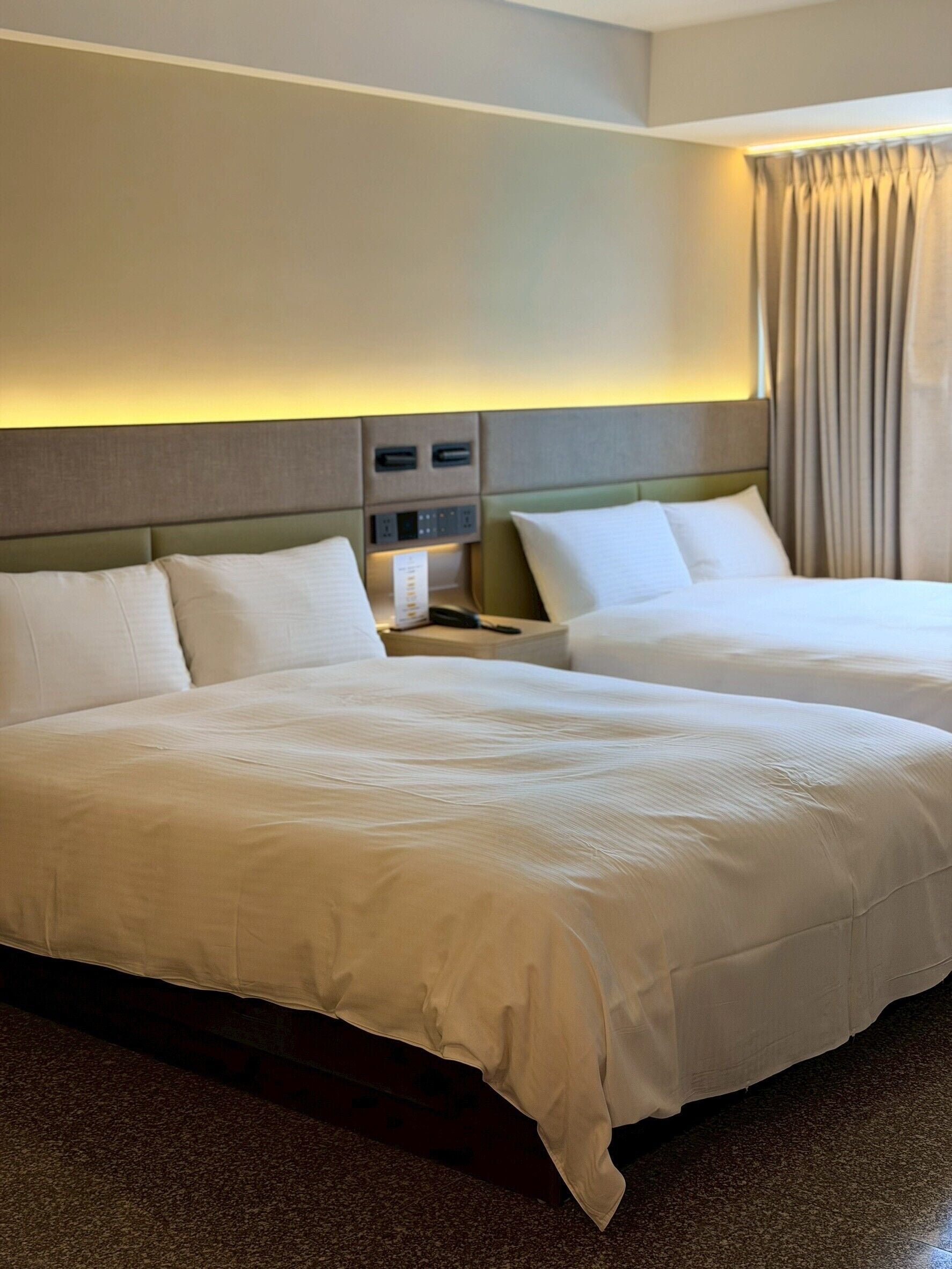 Une chambre d’hôtel avec deux lits, une table de chevet avec un téléphone et une tête de lit dotée d’un éclairage intégré.