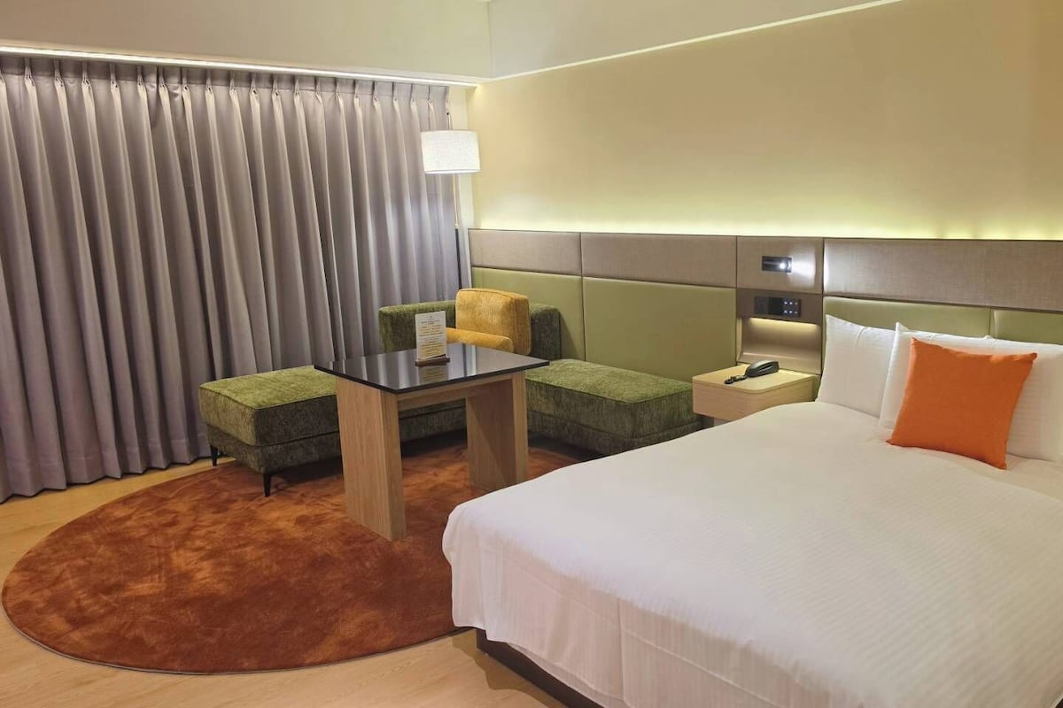 Une chambre d’hôtel avec un lit, un bureau, une chaise, une table de chevet et une lampe.