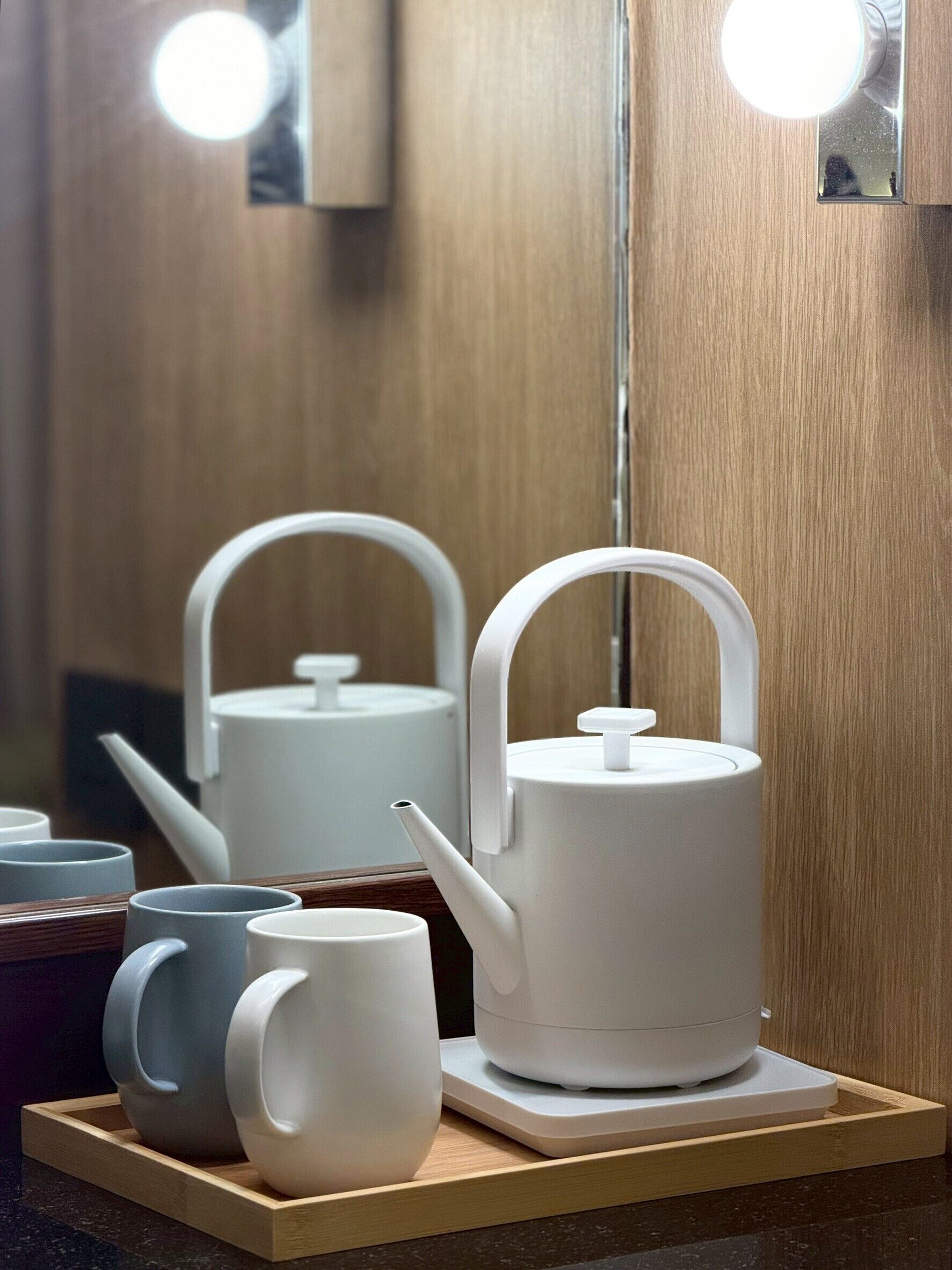 A tea set on a tray with a wooden surface, a mirror with lights, and a wooden wall.