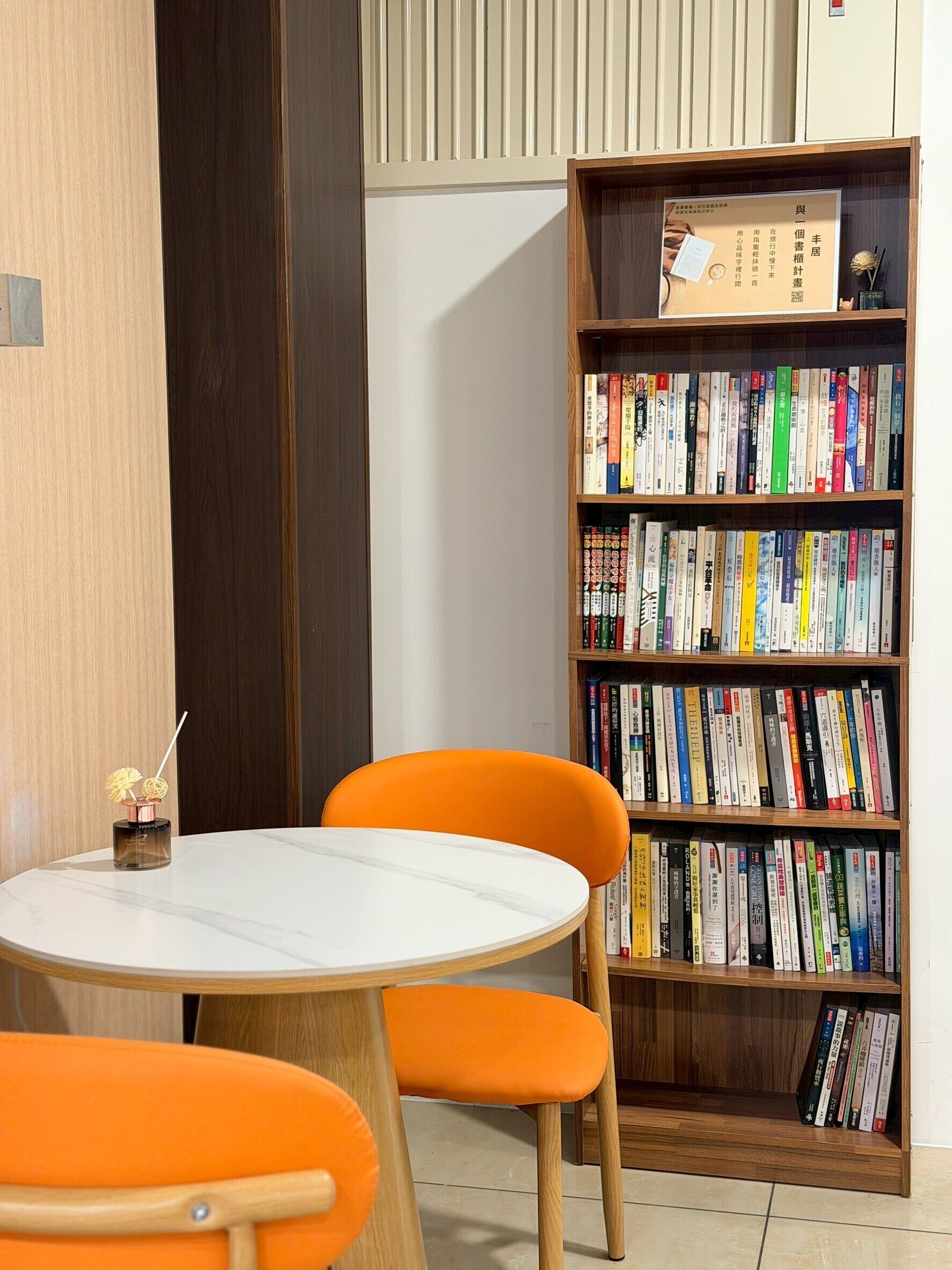 A room with a round table, two orange chairs, a bookshelf filled with books, and a wooden cabinet.