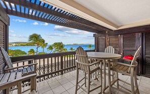 Ein Balkon mit Tisch und Stühlen, der auf einen Strand und den Ozean blickt.