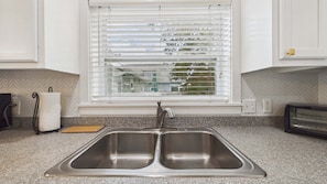 A kitchen with a double stainless steel sink, a window with blinds, and a toaster on the countertop. - Bon Villa 102-Golf Cart + Private Pool-Sleeps 10 (Seagrove Beach)