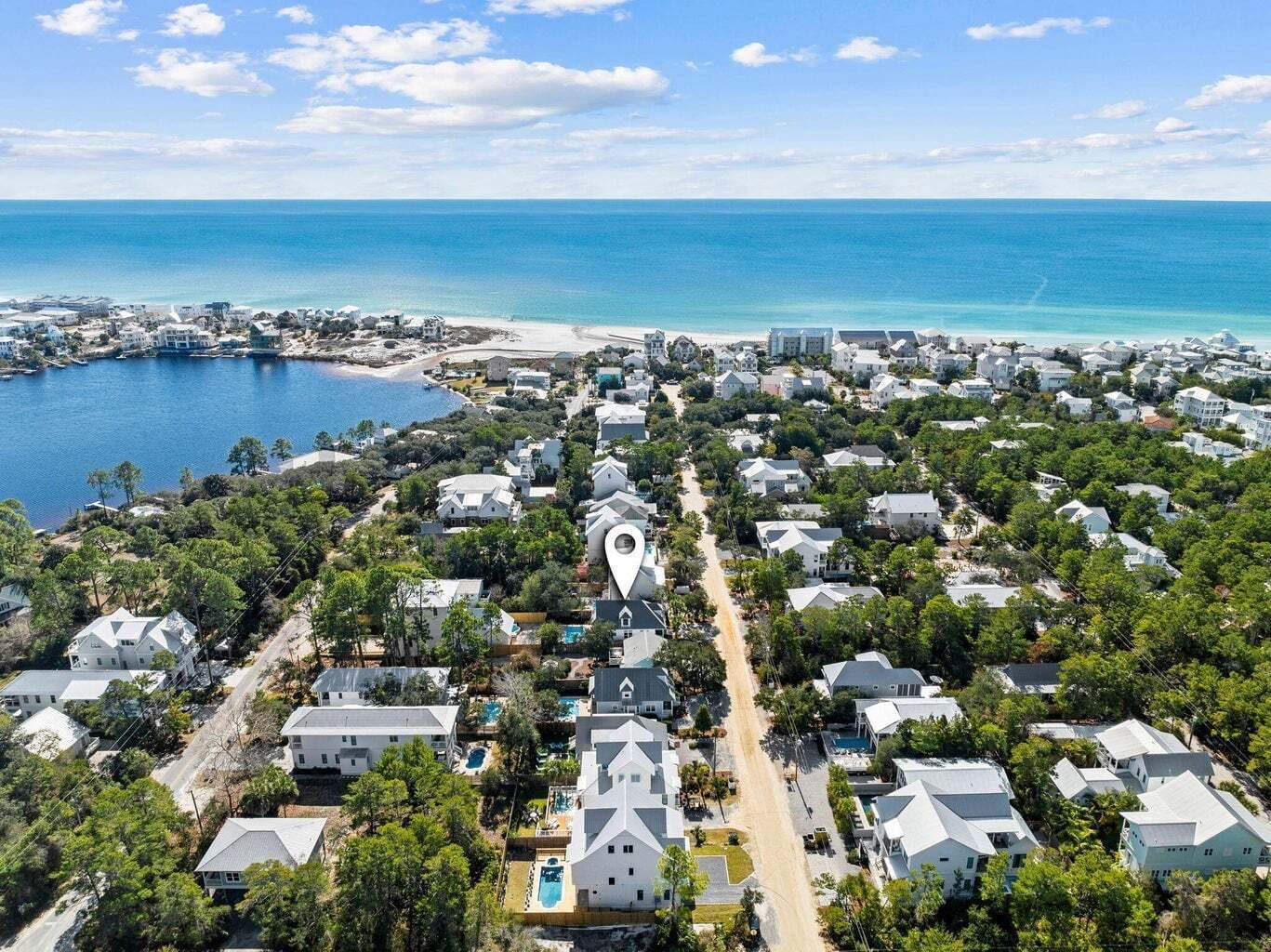 An aerial view of a coastal residential area with houses, a beach, and a marina.