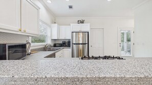 A modern kitchen with white cabinetry, a stainless steel refrigerator, a built-in oven, and a granite countertop. - Bon Villa 102-Golf Cart + Private Pool-Sleeps 10 (Seagrove Beach)