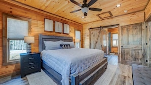 A wooden cabin bedroom with a bed, nightstands, a ceiling fan, and a large wooden door. - Riverfront cabin in lovely gated community with hot tub and game room (Ellijay)