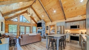 A spacious log cabin with a large living area, a stone fireplace, and a kitchen with modern appliances. - Riverfront cabin in lovely gated community with hot tub and game room (Ellijay)