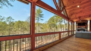 A wooden deck with large windows overlooking a forested area. - Riverfront cabin in lovely gated community with hot tub and game room (Ellijay)