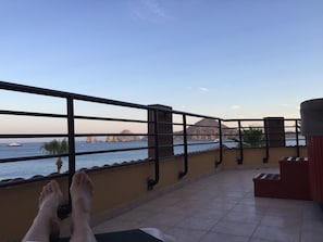 Ein Balkon mit Blick auf das Meer, eine Palme und ein Berg in der Ferne.