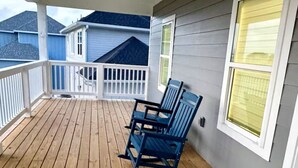 Eine Holzterrasse mit weißer Reling, zwei Schaukelstühlen und Blick auf angrenzende Häuser.