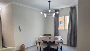 En matplats med ett runt bord och fyra stolar, en hängande lampa och ett fönster med gardiner.