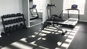 A gym with exercise equipment, a treadmill, and a mirror reflecting the room. - Beachy Vibes Retreat -7HP (Laguna Vista)