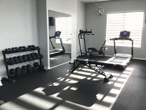 Ein Fitnessraum mit Trainingsgeräten, einem Laufband und einem Spiegel, der den Raum wiedergibt.