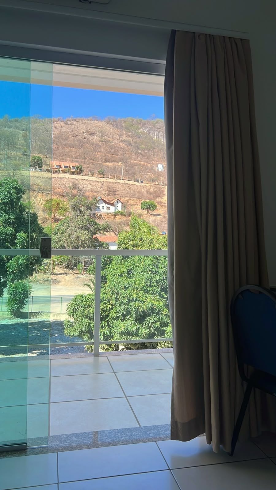 Una habitación con puerta corrediza de vidrio que da a un balcón con vistas a un paisaje montañoso y algunas casas.